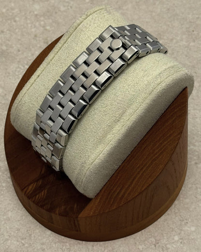 PB TimePiece stainless steel flat jubilee bracelet with hidden clasp displayed on a wooden watch stand