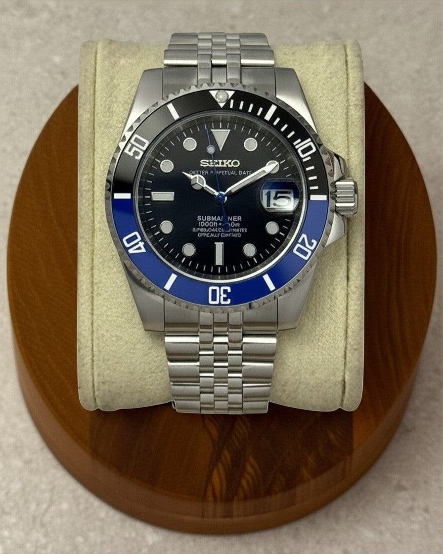 PB TimePiece Submariner Batman watch with black and blue bezel, black dial, and stainless steel jubilee bracelet.