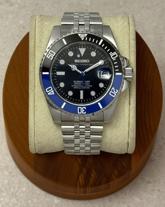 PB TimePiece Submariner Batman watch with black and blue bezel, black dial, and stainless steel jubilee bracelet.