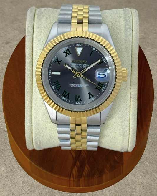PB TimePiece two-tone gold watch with a black Wimbledon dial, fluted bezel, and jubilee bracelet on a display stand.