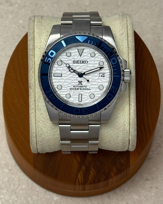 PB TimePiece Yachtmaster watch with a white wave-textured dial, navy blue bezel, and stainless steel oyster bracelet.